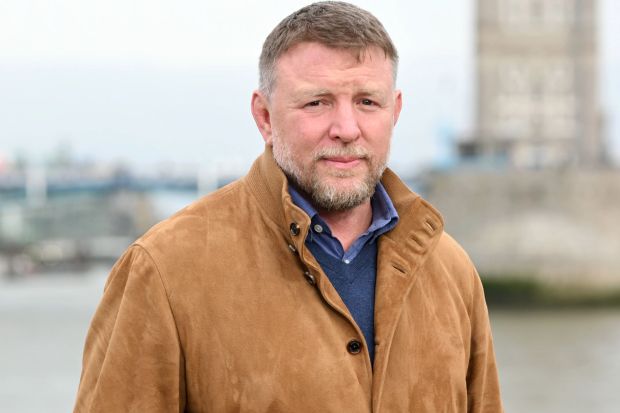 a man in a brown jacket stands in front of a body of water