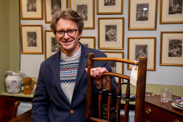 a man in a blue jacket holds a wooden chair