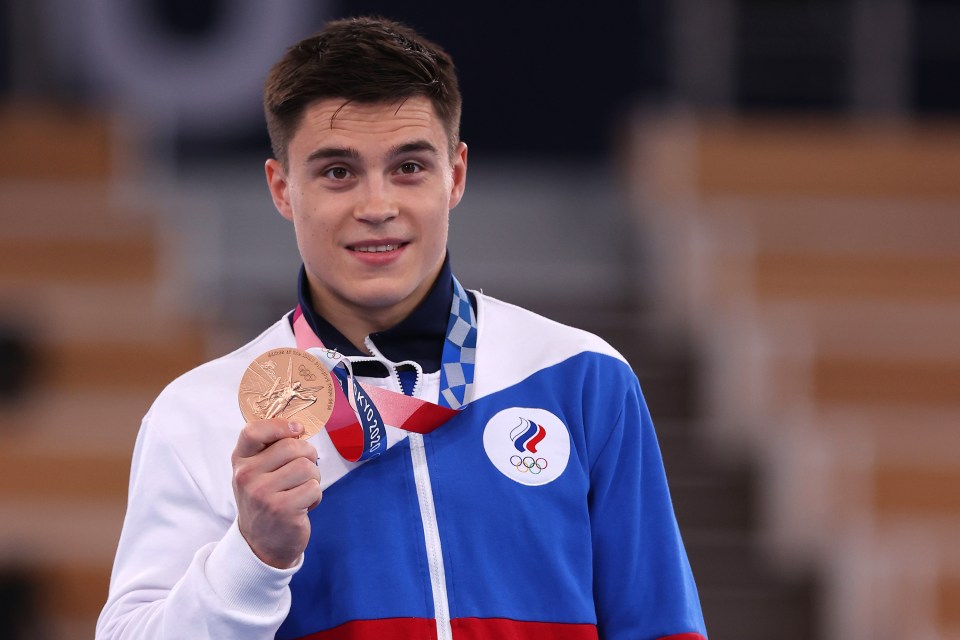 a man in a blue and white olympics jacket holds up a gold medal