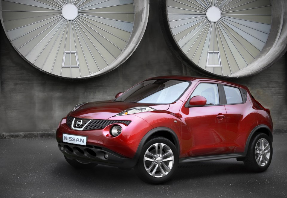 a red nissan juke is parked in front of a building