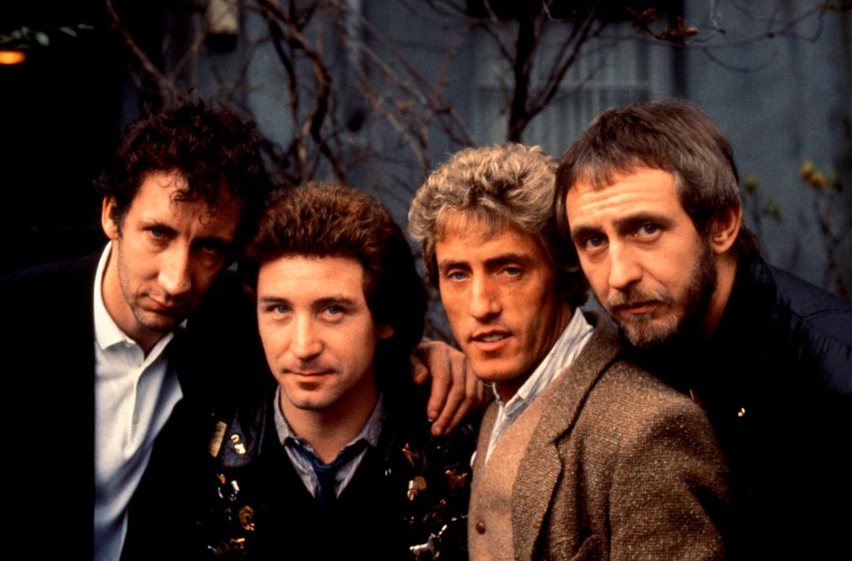 four men are posing for a picture and one has a badge on his jacket