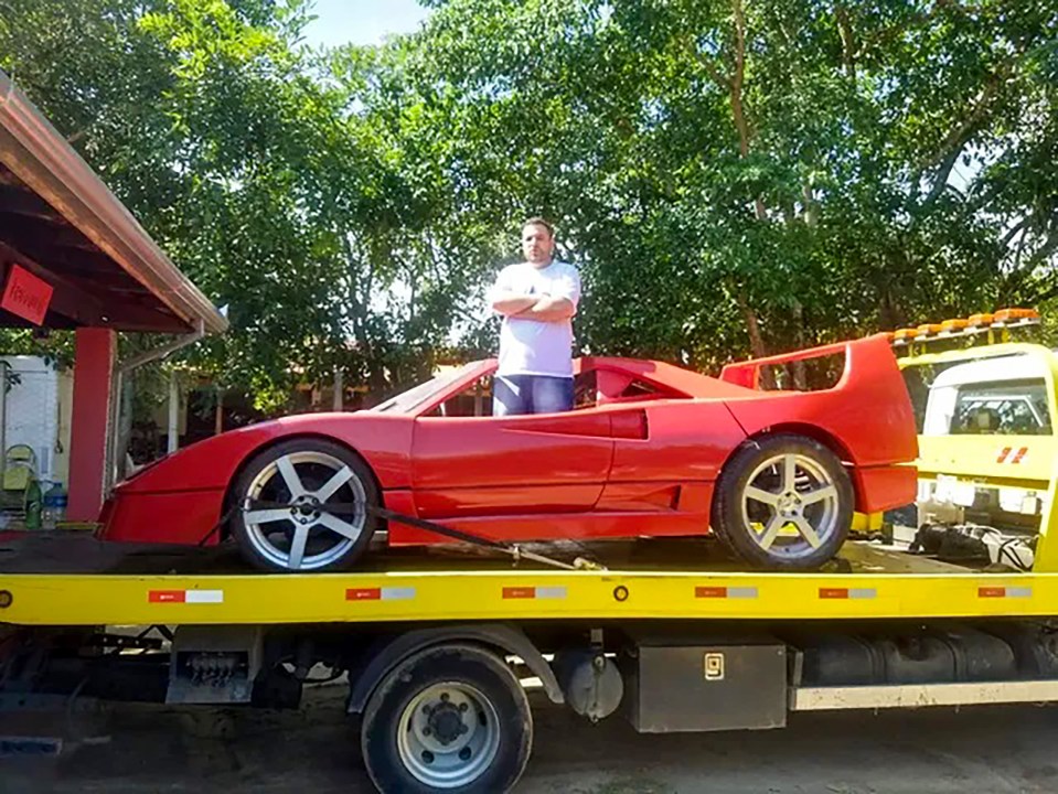 a man stands next to a red sports car on a yellow tow truck