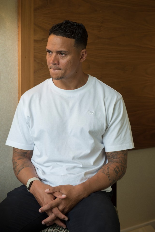 a man wearing a white new balance shirt sits with his hands folded