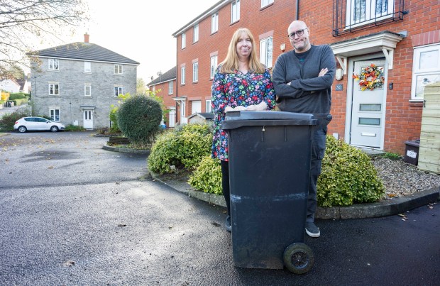 a man and a woman standing next to a trash can in front of a house