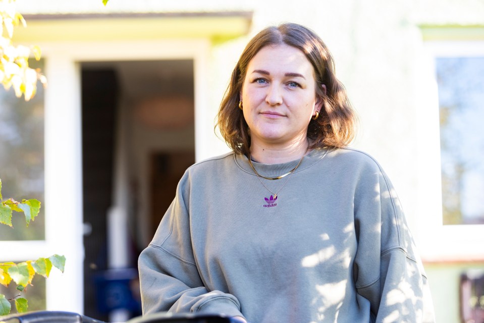 a woman wearing an adidas sweatshirt stands in front of a house