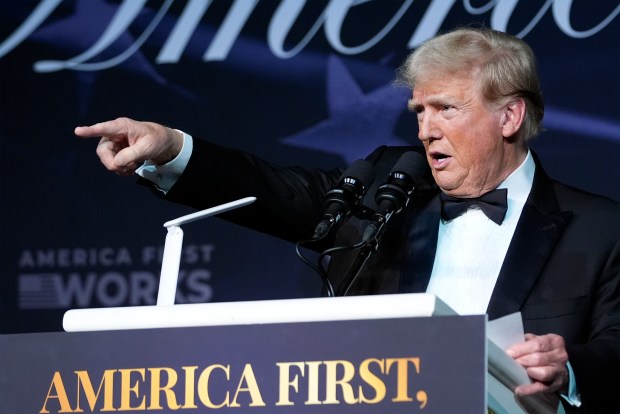 a man in a tuxedo stands at a podium that says america first