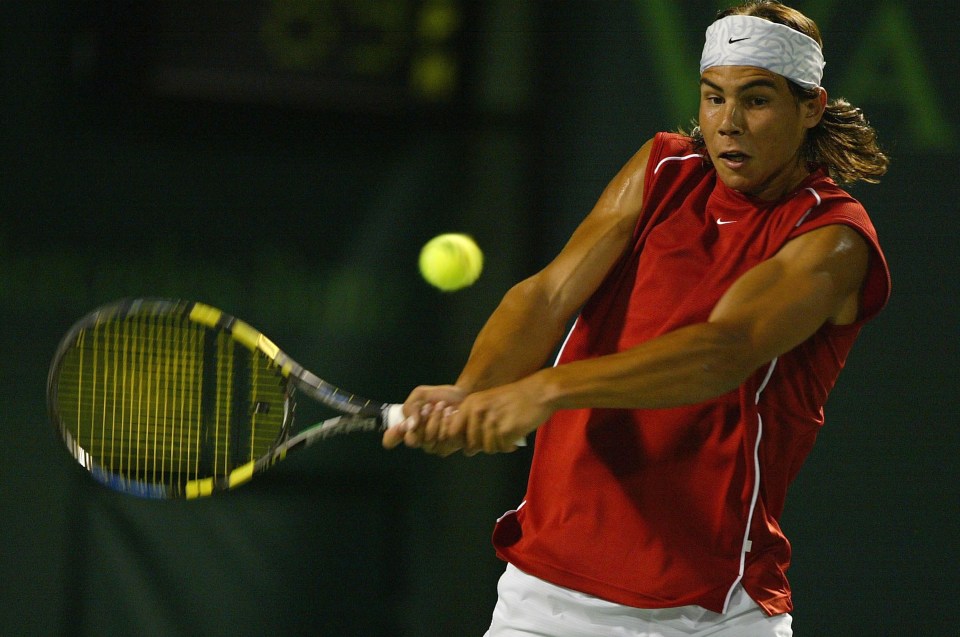 a man in a red shirt is swinging a tennis racket at a tennis ball