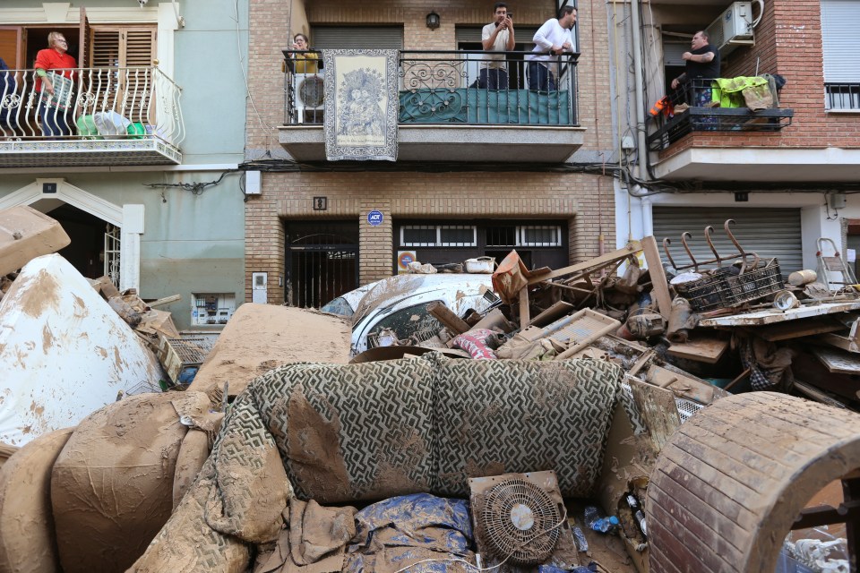 Residents stand on their balconies above destroyed furniture below after the deadly floods