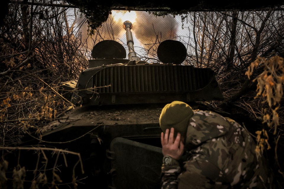 a man in a yellow hat looks at a military vehicle