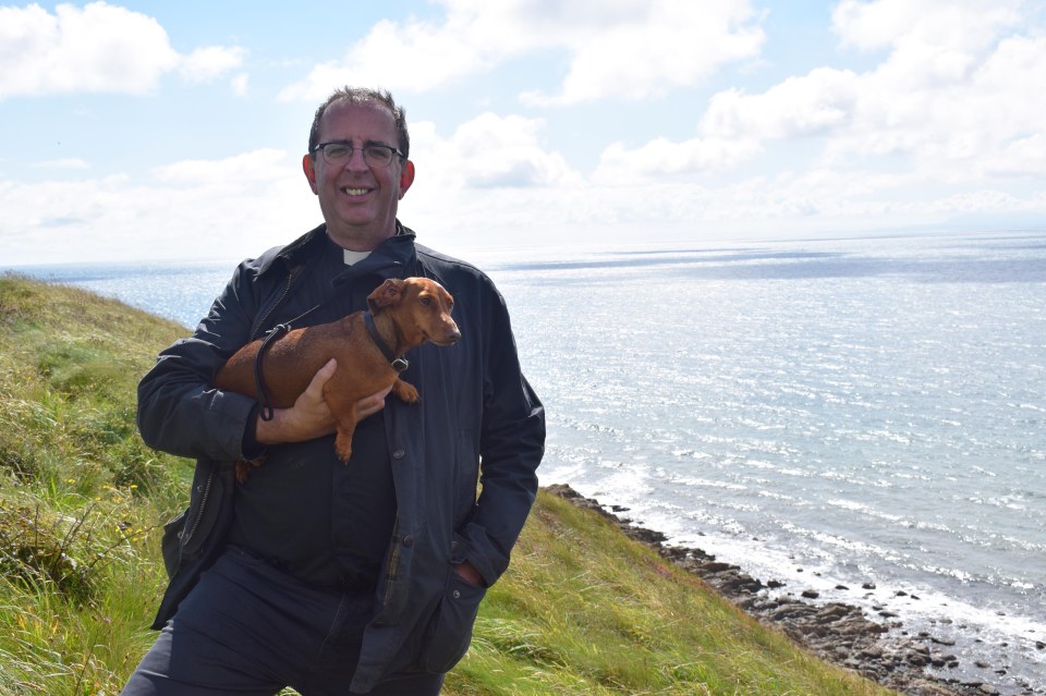 a man holds a small brown dog in his arms in front of the ocean