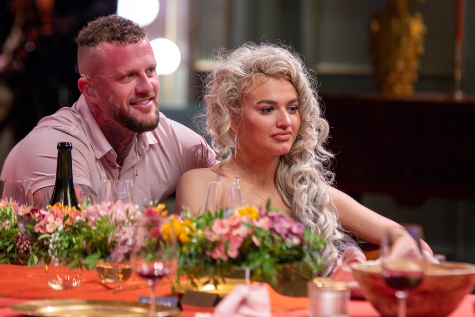 a man and woman sit at a table with flowers and wine glasses