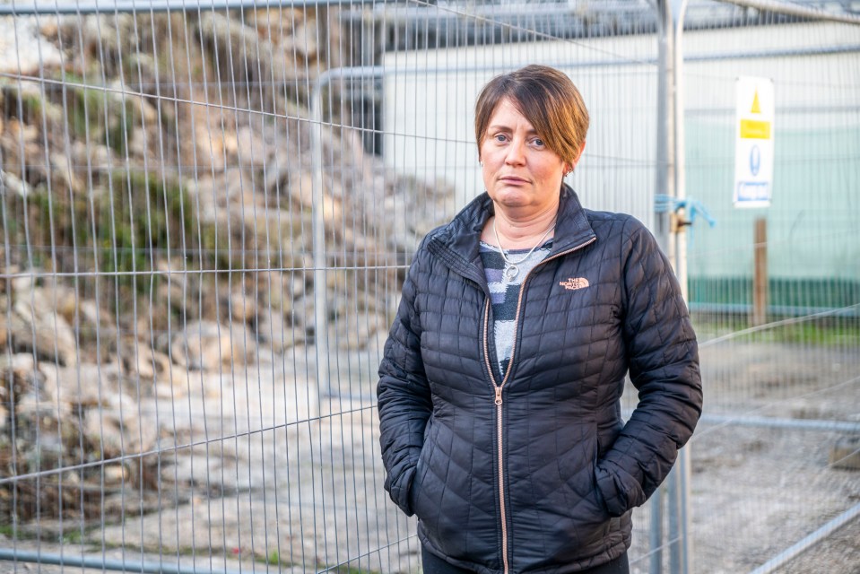 a woman wearing a north face jacket stands in front of a fence