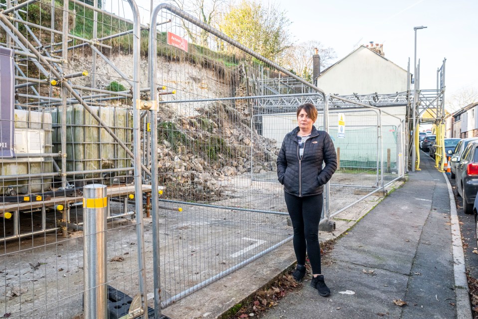 a woman stands in front of a fence with a red sign on it