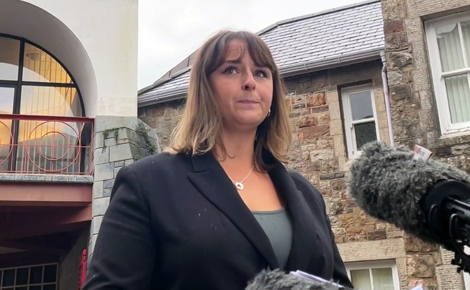 a woman in a black suit stands in front of microphones