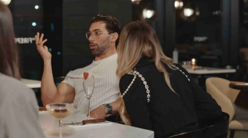 a man and woman are sitting at a table with a glass of wine