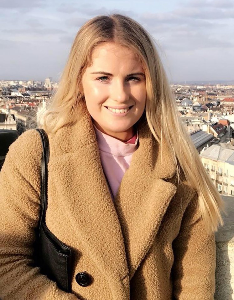 a woman in a brown coat smiles in front of a city