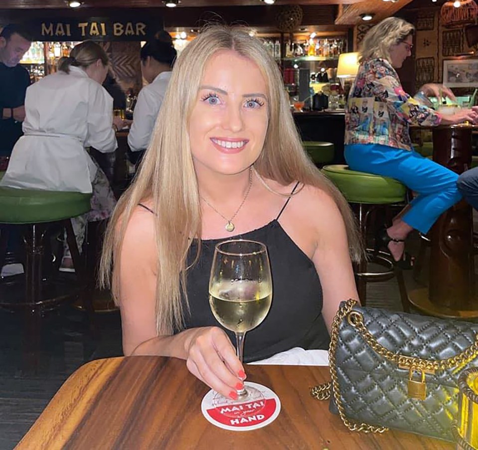 a woman sits at a table with a mai tai bar sign behind her