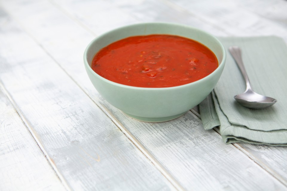 a bowl of tomato soup sits on a table next to a spoon