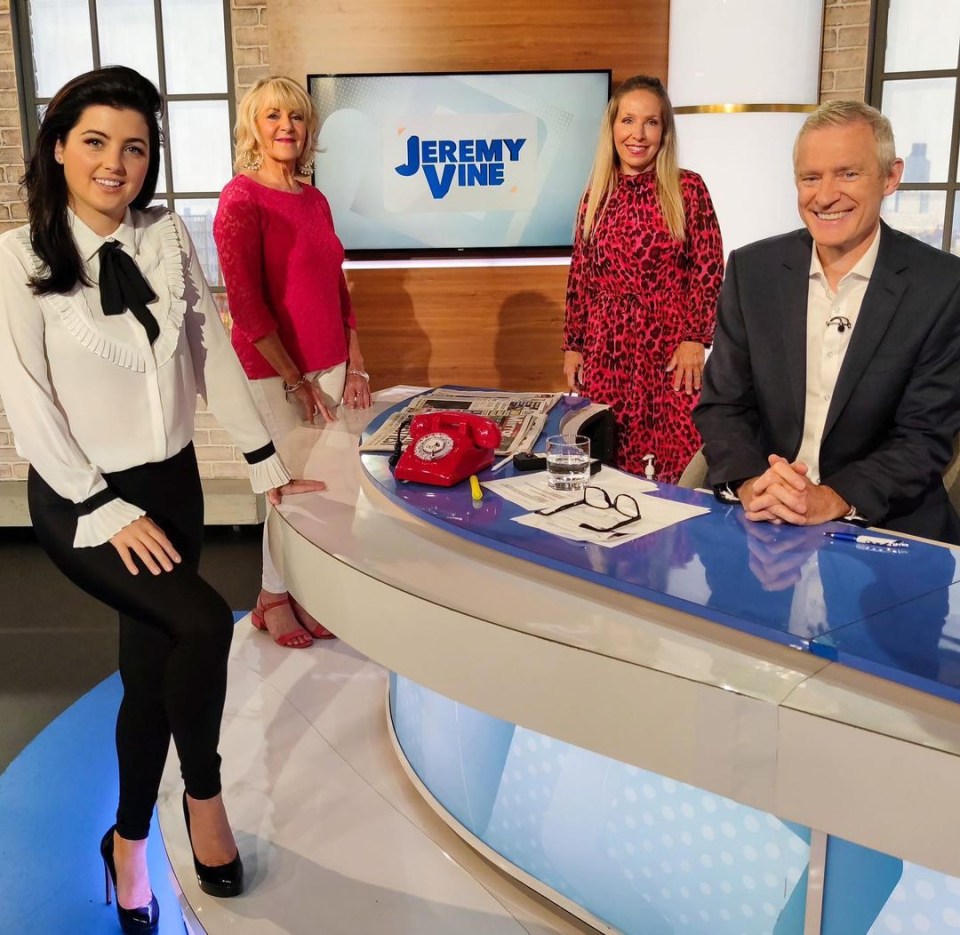 a group of people sitting at a table with jeremy vine on the screen behind them