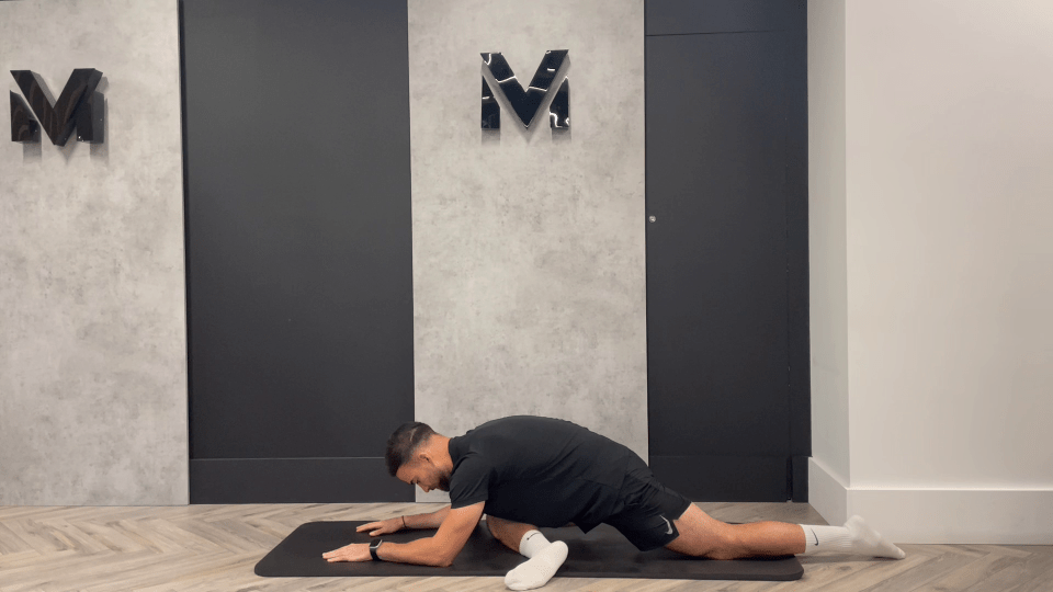 a man is stretching on a mat in front of a wall with the letter m on it