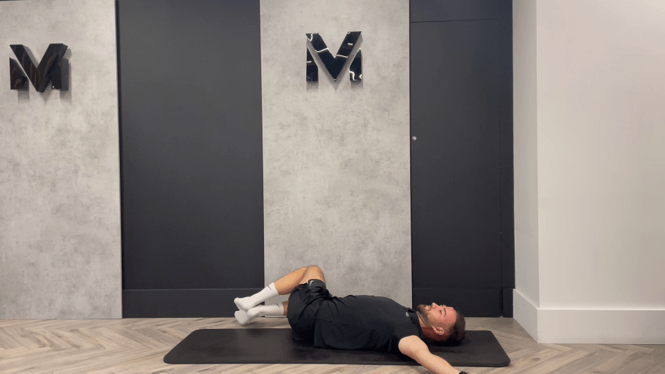 a man is laying on a mat in front of a wall with the letter m on it