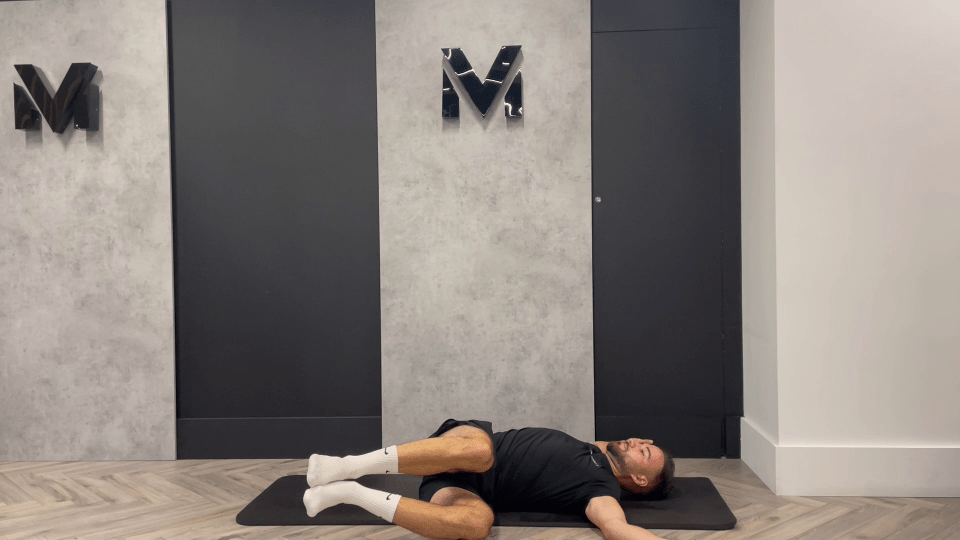 a man is laying on a mat in front of a wall with the letter m on it