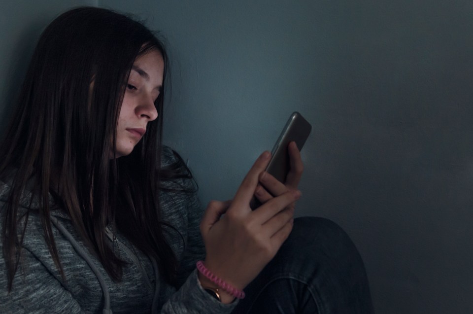 a girl sitting in a corner looking at her phone