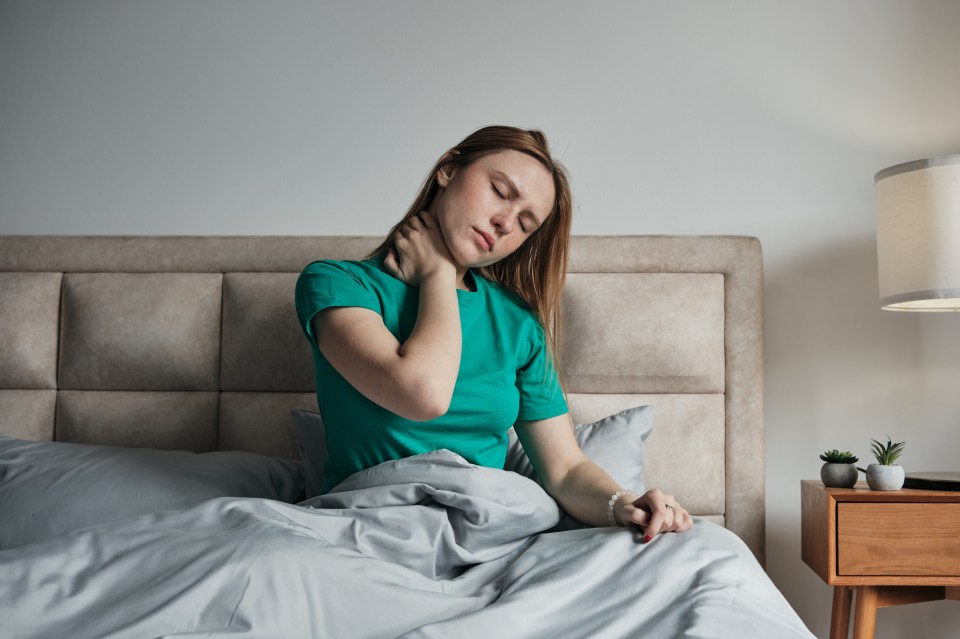 a woman in a green shirt is sitting on a bed holding her neck