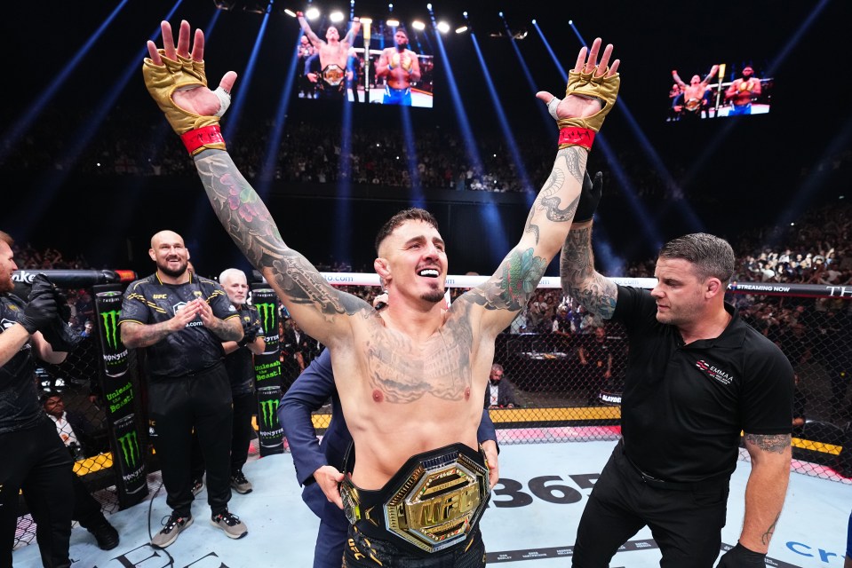 a man in a ufc belt holds his arms in the air