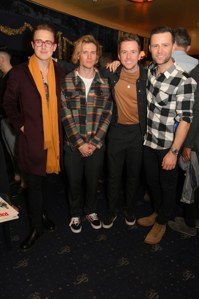 four men posing for a picture with one wearing a plaid shirt