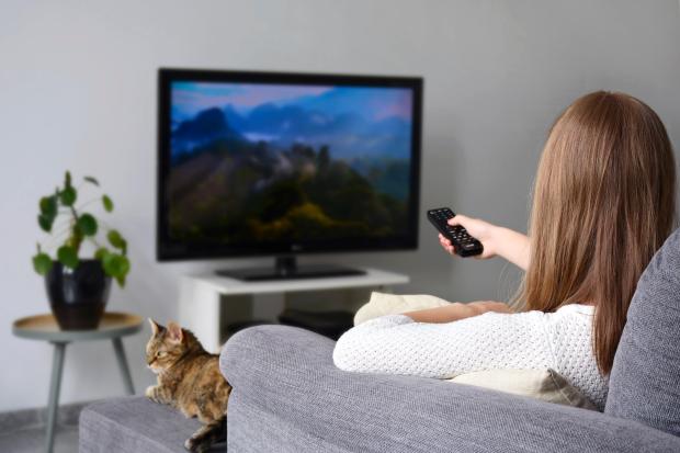 a woman sits on a couch holding a remote control in front of a tv