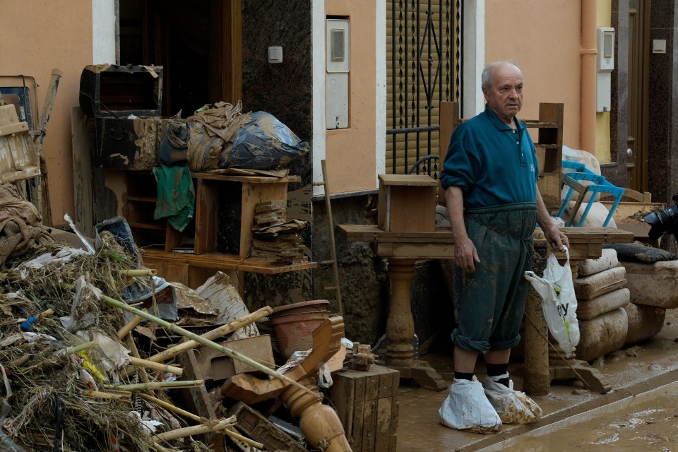 a man in overalls stands in front of a pile of junk