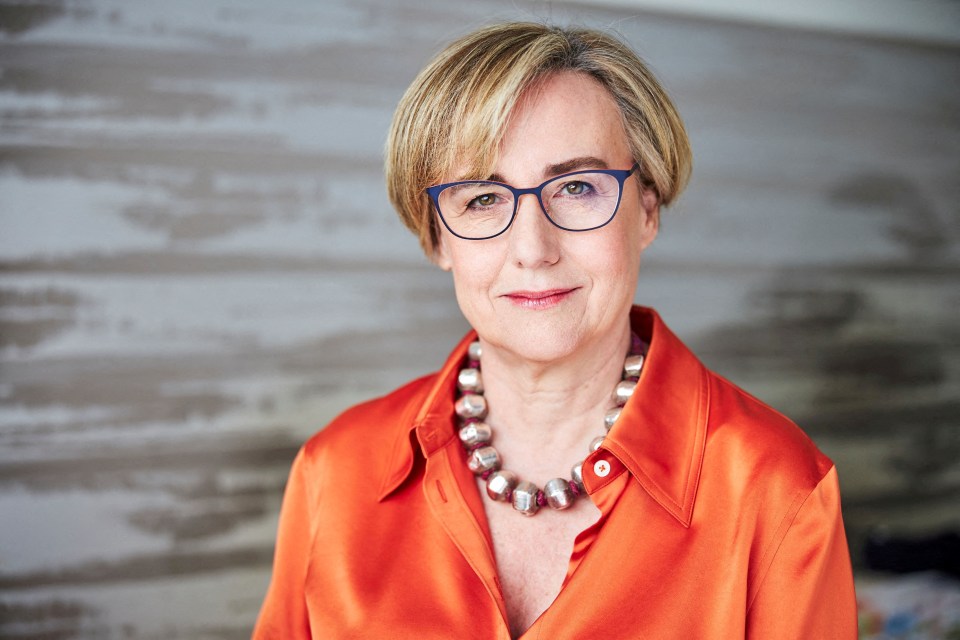 a woman wearing glasses and an orange shirt looks at the camera