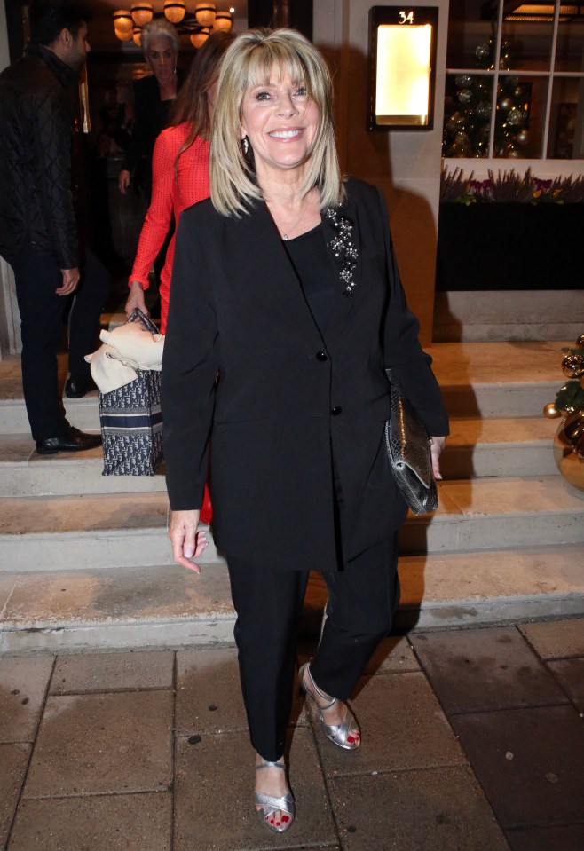 a woman in a black suit is smiling and holding a dior bag