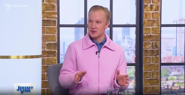 a man in a pink jacket is sitting in a chair on a television show .