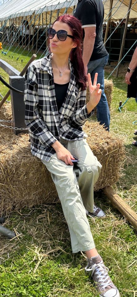 a woman sitting on a bale of hay giving a peace sign