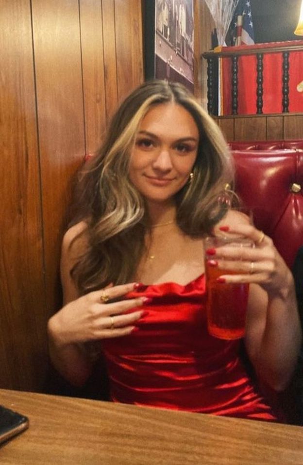 a woman in a red dress is sitting at a table holding a drink .