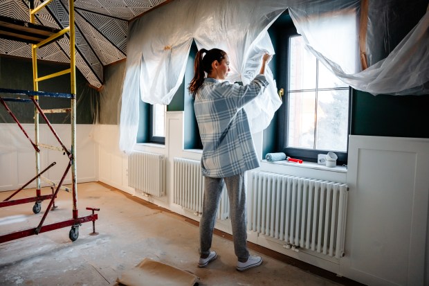 a woman in a plaid shirt is covering a window with plastic