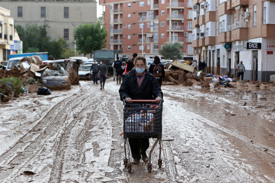 A woman pushes a supermarket trolley with food in a muddy street after floods in Valencia