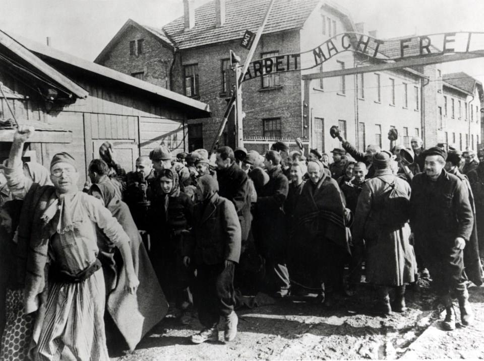 a black and white photo of a group of people standing under a sign that says arbeit macht frei