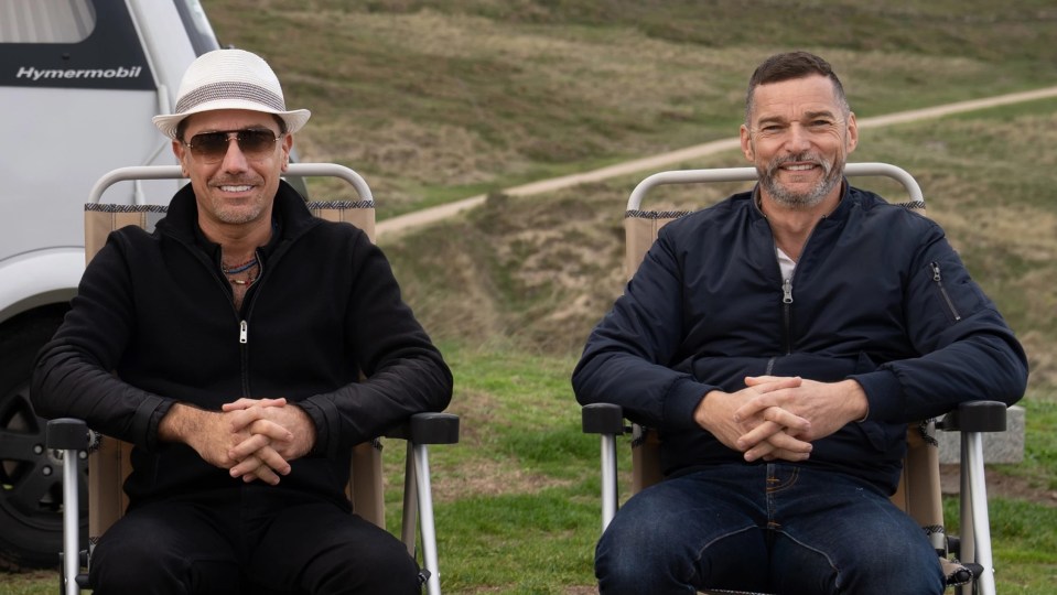 Gino D’Acampo and Fred Sirieix sitting outdoors in camping chairs.