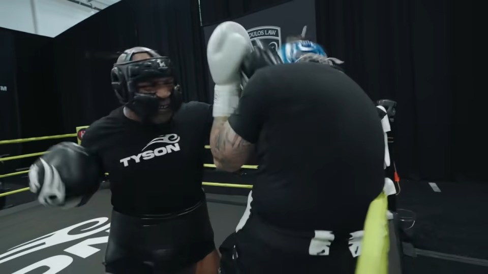 a man wearing a tyson shirt is boxing with another man