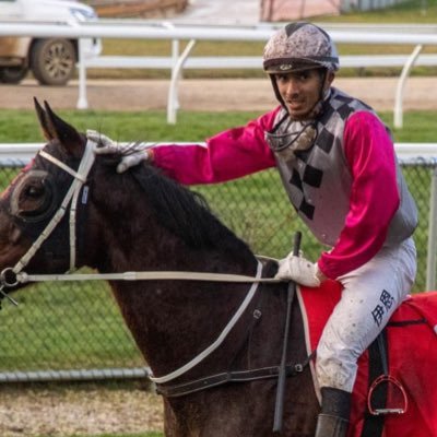 a jockey is riding a black horse on a race track .