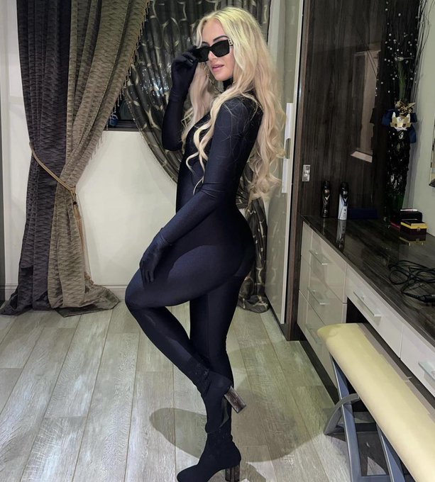 a woman in a black bodysuit and sunglasses stands in a room