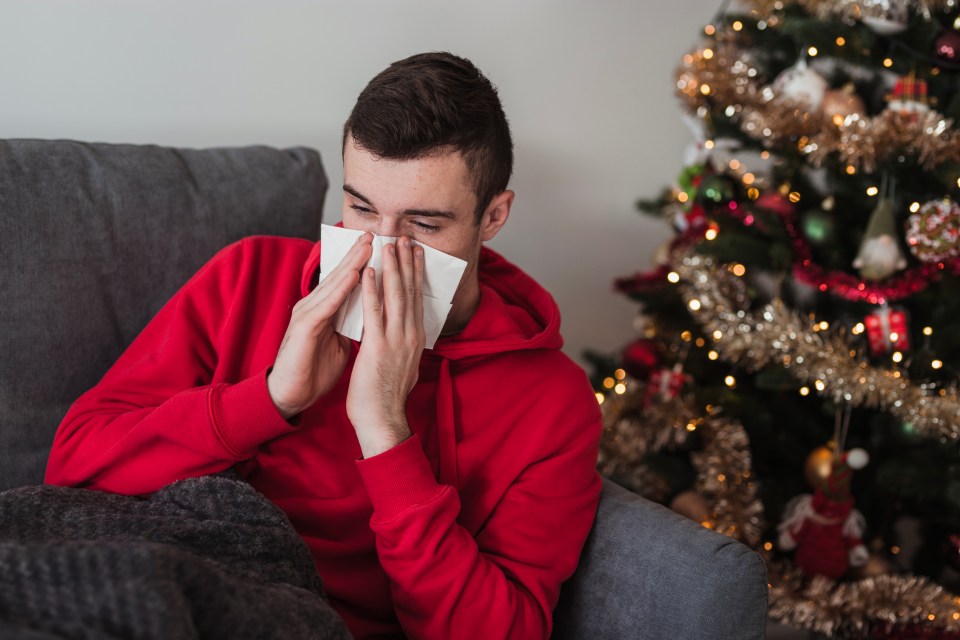 a man blowing his nose in front of a christmas tree