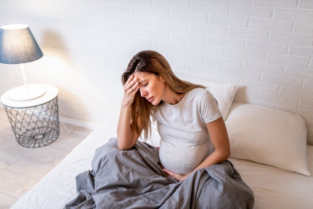 a pregnant woman sits on a bed with her hand on her forehead