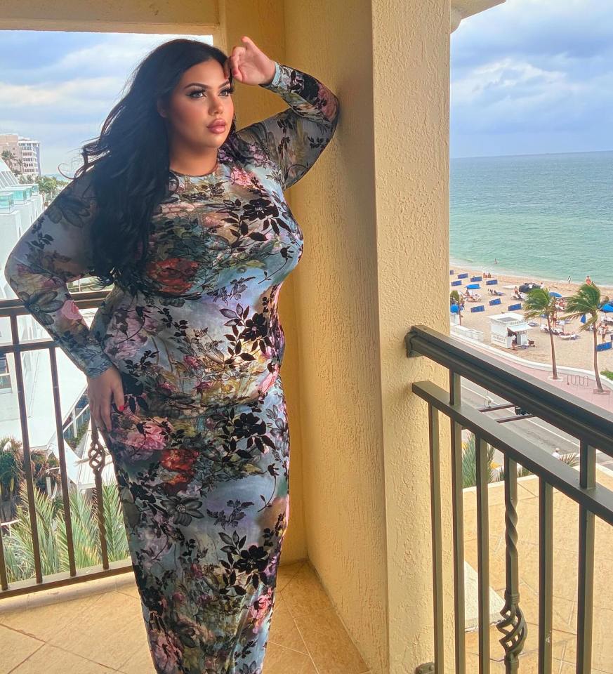 Plus-size influencer on balcony overlooking beach, wearing floral maxi dress.