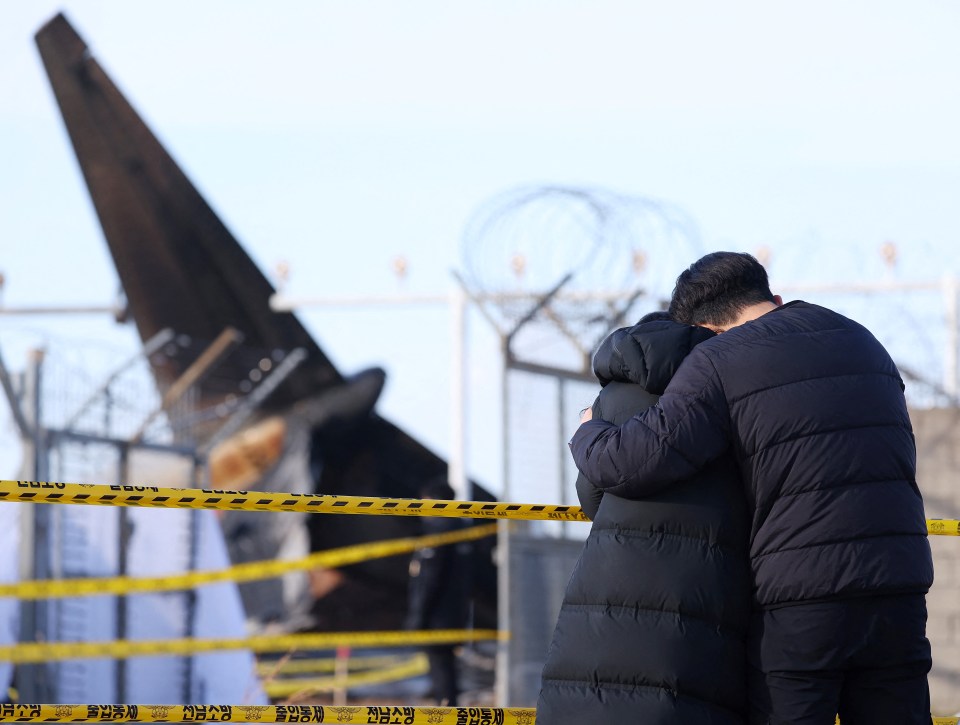 Mourners embrace near the wreckage of a plane crash.