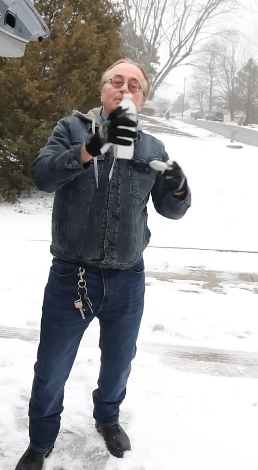 Man in a denim jacket pours liquid from a bottle in snowy weather.