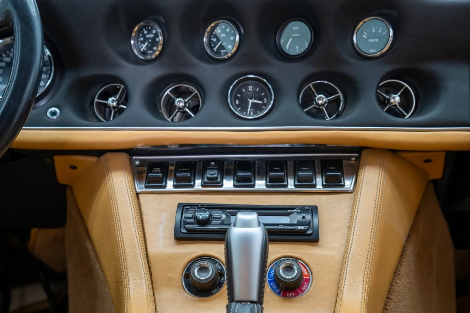 Close-up of a restored 1974 Jensen Interceptor S Cabriolet's interior, showing the dashboard, controls, and tan leather.